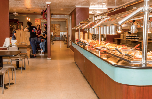 A buffet restaurant with a food display on the right and customers in line on the left. Bright and inviting atmosphere.