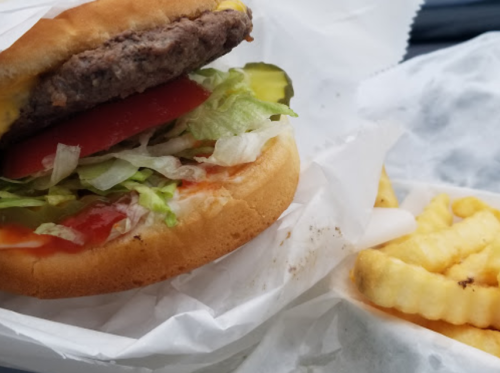A cheeseburger with lettuce, tomato, and pickles beside a serving of crinkle-cut fries in a takeout container.