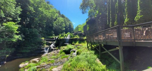 A scenic view of a waterfall surrounded by lush greenery and a wooden deck overlooking the water.