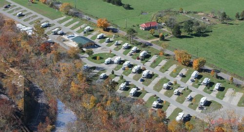 Aerial view of a campground with numerous RVs parked along winding roads, surrounded by trees and open fields.