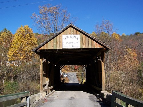 A wooden covered bridge with a sign reading "King Bridge Clearance" surrounded by autumn trees and a clear blue sky.