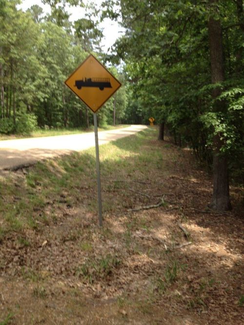 A warning sign for a fire truck on a tree-lined road, with gravel and grass along the roadside.