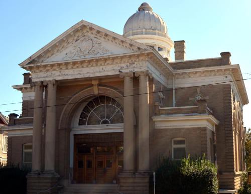 Historic building with a dome, large columns, and ornate architectural details, set against a clear blue sky.