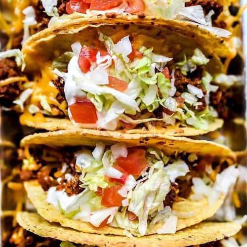 A stack of three tacos filled with ground beef, lettuce, tomatoes, cheese, and sour cream.