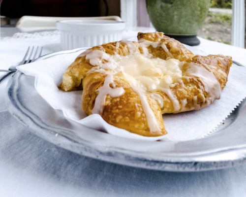 A flaky pastry drizzled with icing, resting on a plate with a white napkin, set on a table.