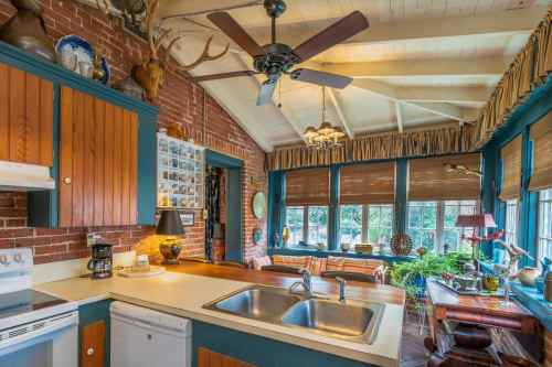 Cozy kitchen with brick walls, wooden cabinets, a ceiling fan, and large windows overlooking a sunny outdoor space.