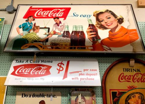 Vintage Coca-Cola advertisements featuring women serving drinks and promotional pricing for cases of soda.