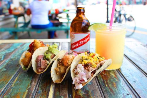 A colorful spread of tacos with various fillings, a bottle of Red Stripe beer, and a refreshing drink with a straw.