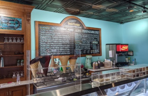 Ice cream shop interior featuring a menu board, ice cream display, and toppings station with a Coca-Cola machine.