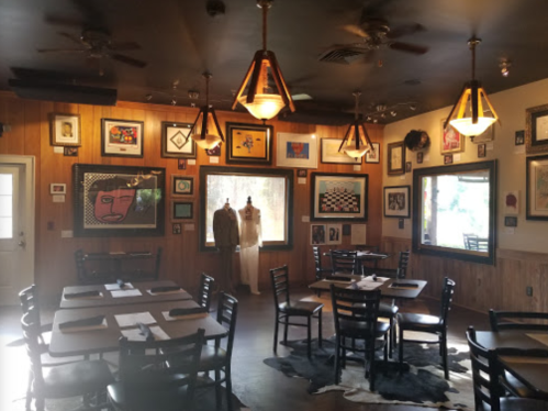 Cozy restaurant interior with wooden walls, art on display, and tables set for dining.