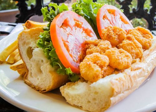 A shrimp po' boy sandwich with lettuce, tomato, and fries on the side, served on a toasted baguette.