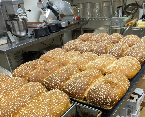 Freshly baked loaves of bread topped with sesame seeds, arranged on trays in a kitchen setting.