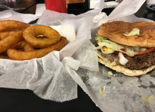 A juicy hamburger with lettuce, tomato, and onions next to a serving of crispy onion rings, both on parchment paper.