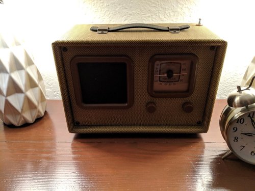 A vintage-style radio with a textured exterior, placed on a wooden surface next to a decorative lamp and clock.
