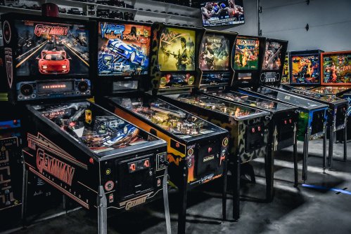 A row of colorful pinball machines in a game room, featuring various themes and designs.
