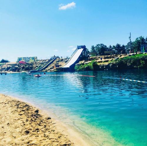 A sunny beach scene featuring a clear blue water area with a water slide and sandy shore in the background.