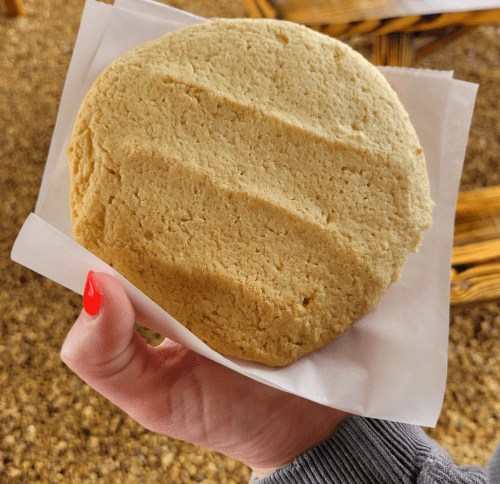 A hand holding a large, round, thick cookie on a piece of white paper, set against a textured background.