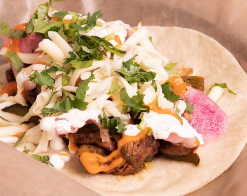 A close-up of a taco filled with meat, cheese, sour cream, and fresh toppings on a soft tortilla.