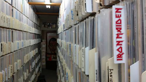 A narrow aisle between shelves filled with vinyl records, featuring labels like "Iron Maiden" and various artists.
