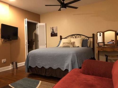 Cozy bedroom with a blue bedspread, a TV on the wall, and a red couch, featuring warm lighting and a mirror.