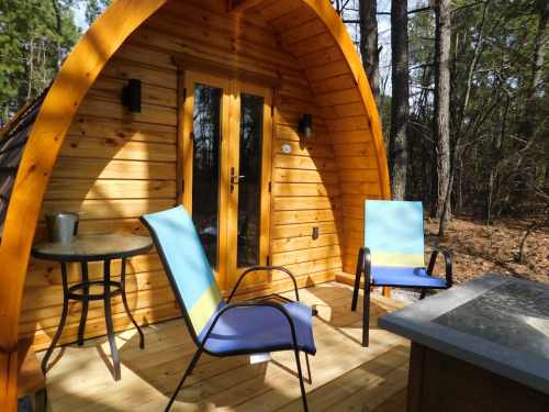 Cozy wooden cabin with two chairs and a small table, surrounded by trees in a serene outdoor setting.