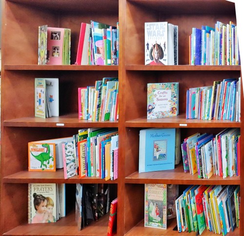 A wooden bookshelf filled with colorful children's books, including titles like "Star Wars" and "Mother Goose."