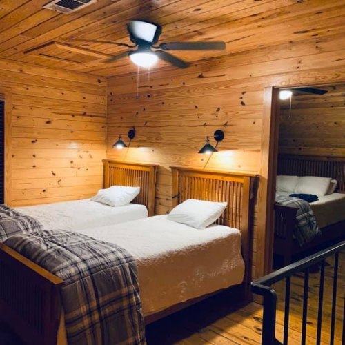 Cozy wooden bedroom with two twin beds, a ceiling fan, and warm lighting, featuring a rustic decor style.