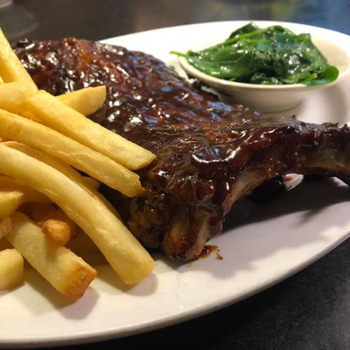 A plate featuring BBQ ribs, golden French fries, and a side of sautéed spinach.