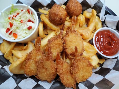 A basket of fried shrimp, French fries, hushpuppies, coleslaw, and ketchup on a checkered paper liner.