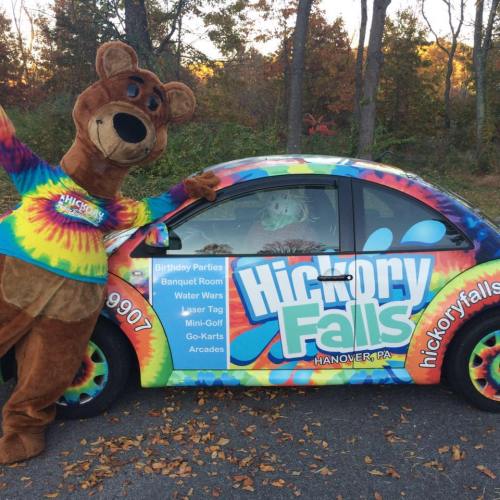 A colorful car with a bear mascot promoting Hickory Falls attractions in Hanover, PA, surrounded by autumn foliage.