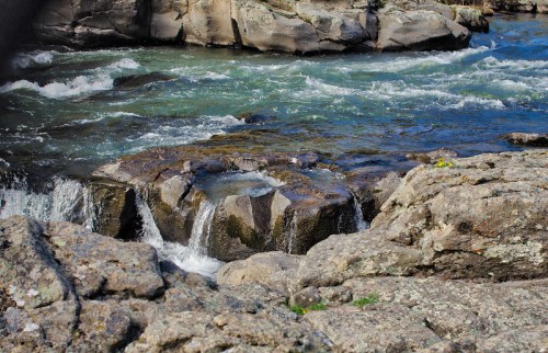 A rocky riverbank with flowing water and small waterfalls cascading over stones.