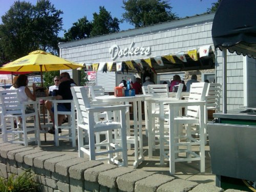Outdoor dining area with white tables and chairs, colorful umbrellas, and a casual eatery in the background.