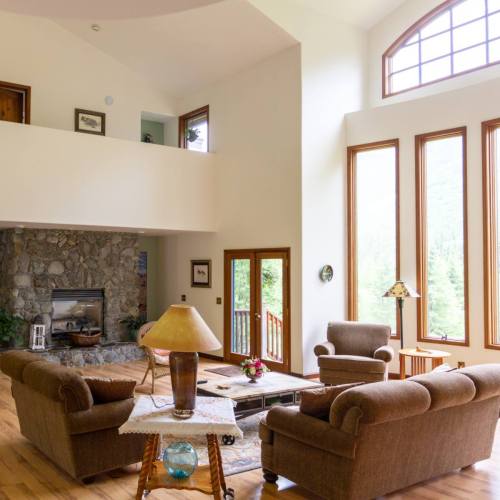 Spacious living room with large windows, stone fireplace, and cozy seating arrangements. Natural light fills the space.