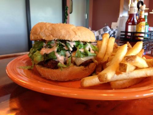 A burger with lettuce and sauce on a bun, served with a side of golden French fries on an orange plate.