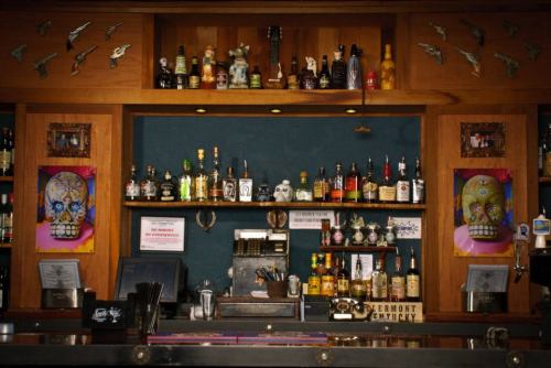 A bar shelf displaying various bottles, decorated with colorful skull art and vintage items against a wooden backdrop.