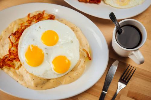 A plate of creamy gravy with three sunny-side-up eggs, crispy hash browns, and a cup of black coffee on the side.