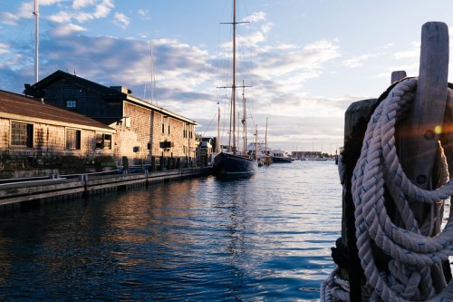 A serene harbor scene at sunset, featuring boats, wooden buildings, and a rope coiled on a dock.
