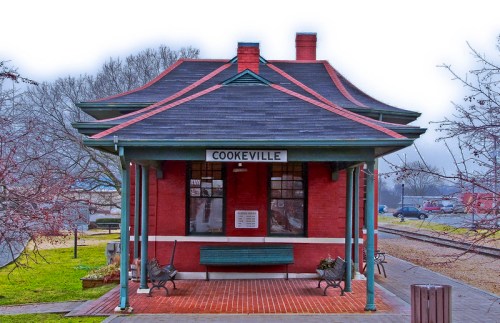 Historic Cookeville train station with a red brick facade and green accents, surrounded by trees and a foggy atmosphere.