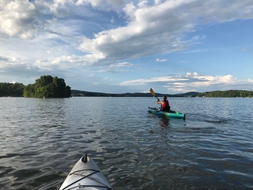A person kayaking on a calm lake with a cloudy sky and distant trees in the background.