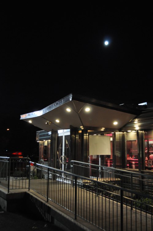 A modern diner illuminated at night, with a bright moon overhead and a welcoming entrance.
