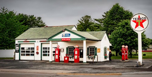 Historic Texaco gas station with vintage pumps, located on Route 66, surrounded by green trees under a cloudy sky.