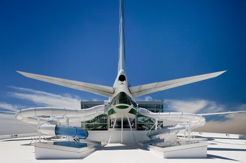 A futuristic building with a large, wing-like structure and sleek design against a clear blue sky.