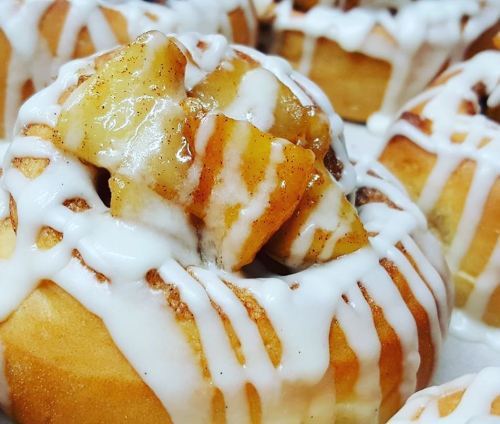 Close-up of a cinnamon roll topped with glazed apples and drizzled with white icing.
