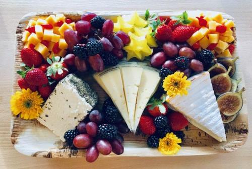 A colorful cheese platter featuring various cheeses, fruits like grapes and strawberries, and decorative flowers.