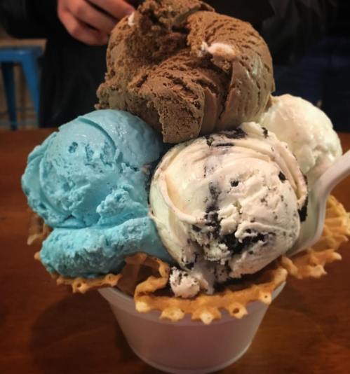 A colorful ice cream sundae in a waffle bowl, featuring blue, white, and brown scoops of ice cream.