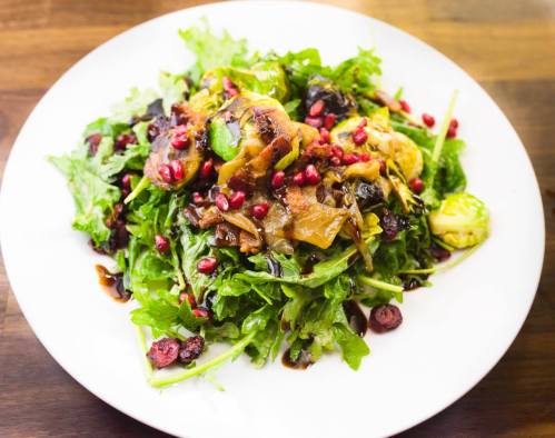 A vibrant salad with mixed greens, pomegranate seeds, and a savory dressing, served on a white plate.