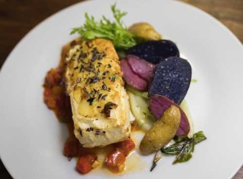 A plated dish featuring baked fish with herbs, served with colorful potatoes and vegetables on a white plate.