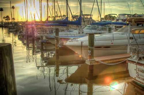 Sunset over a marina filled with boats, reflecting on calm water, with masts silhouetted against the colorful sky.