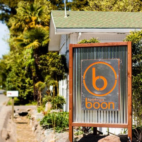 Sign for "boon hotel + spa" featuring a circular logo, surrounded by greenery and a pathway.