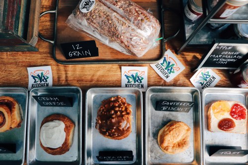 A display of baked goods including bread, pastries, and biscuits, with labels on metal trays.